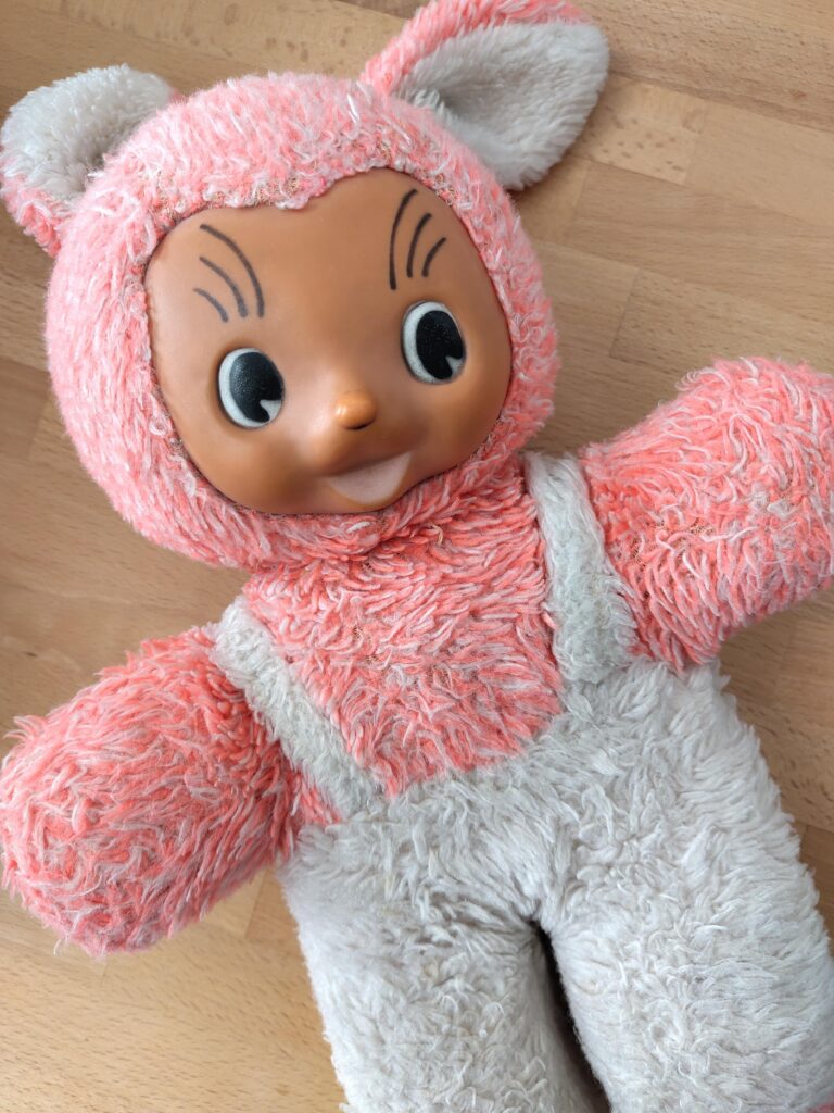 Plüschtier in Neonrosa mit weißer Latzhose und Plastikgesicht